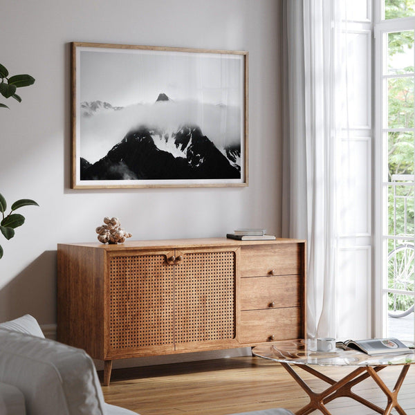 Dramatic black and white landscape of a peak in Alaska, its top rising above a layer of clouds.