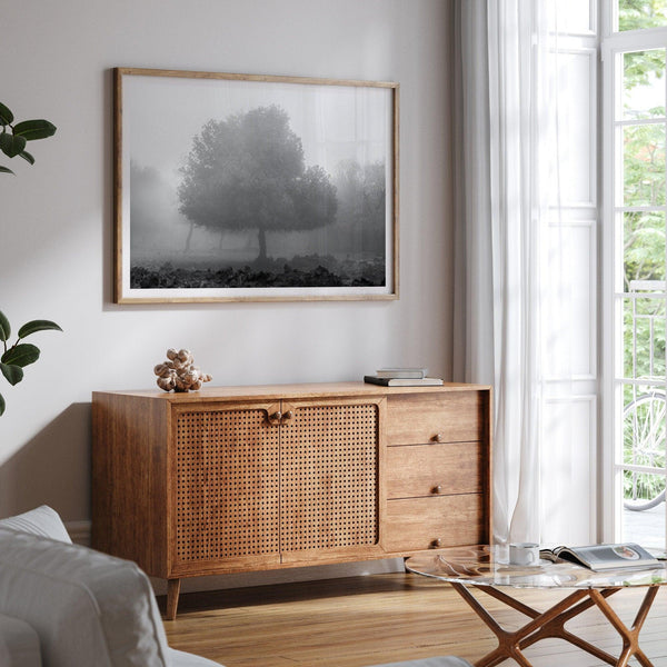 Black and white minimalist fine art photography print of a single tree shrouded in mist. This moody landscape captures the serenity and mystery of a foggy forest, creating a calming and peaceful atmosphere