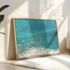 Aerial ocean canvas print showing a lone surfer paddling through turquoise waves with white surf along the beach shoreline