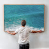 Aerial ocean canvas print showing a lone surfer paddling through turquoise waves with white surf along the beach shoreline