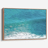 Aerial ocean canvas print showing a lone surfer paddling through turquoise waves with white surf along the beach shoreline