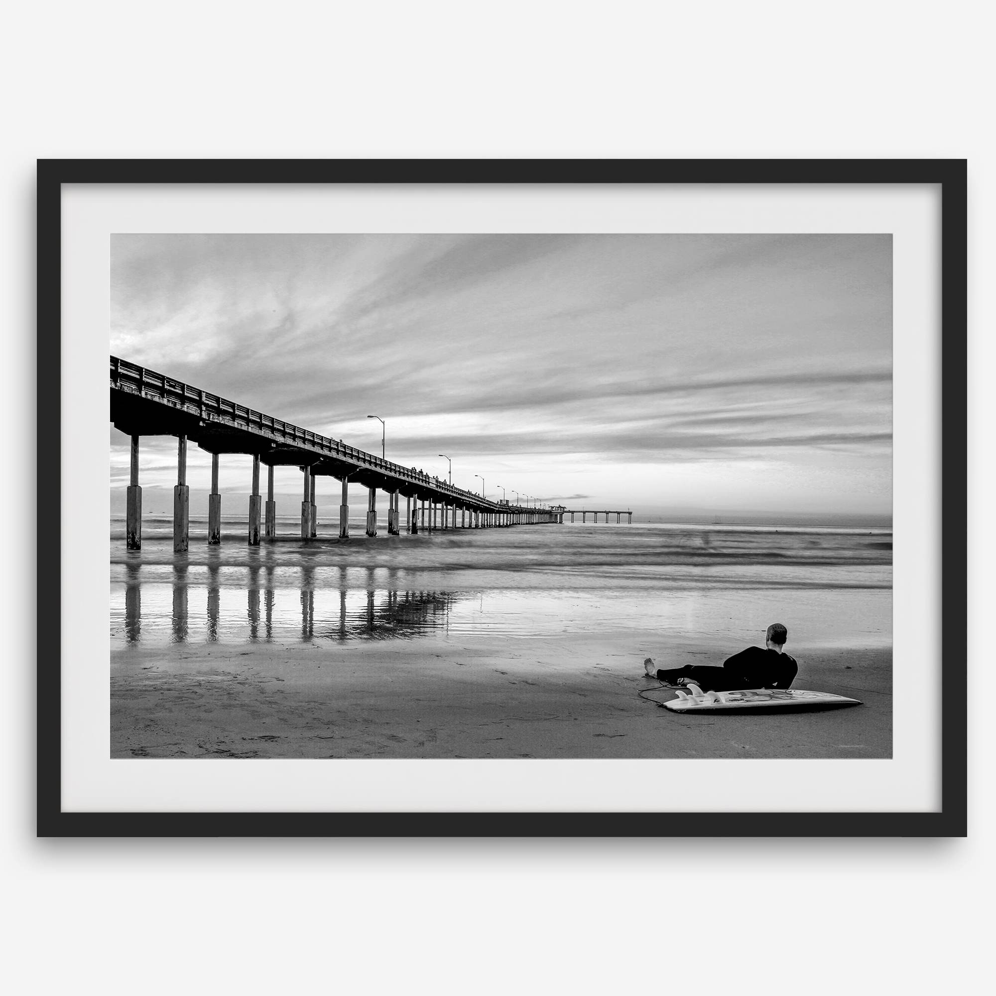 Ocean Beach Pier San Diego photographed in black and white with a lone surfer resting on the shoreline.