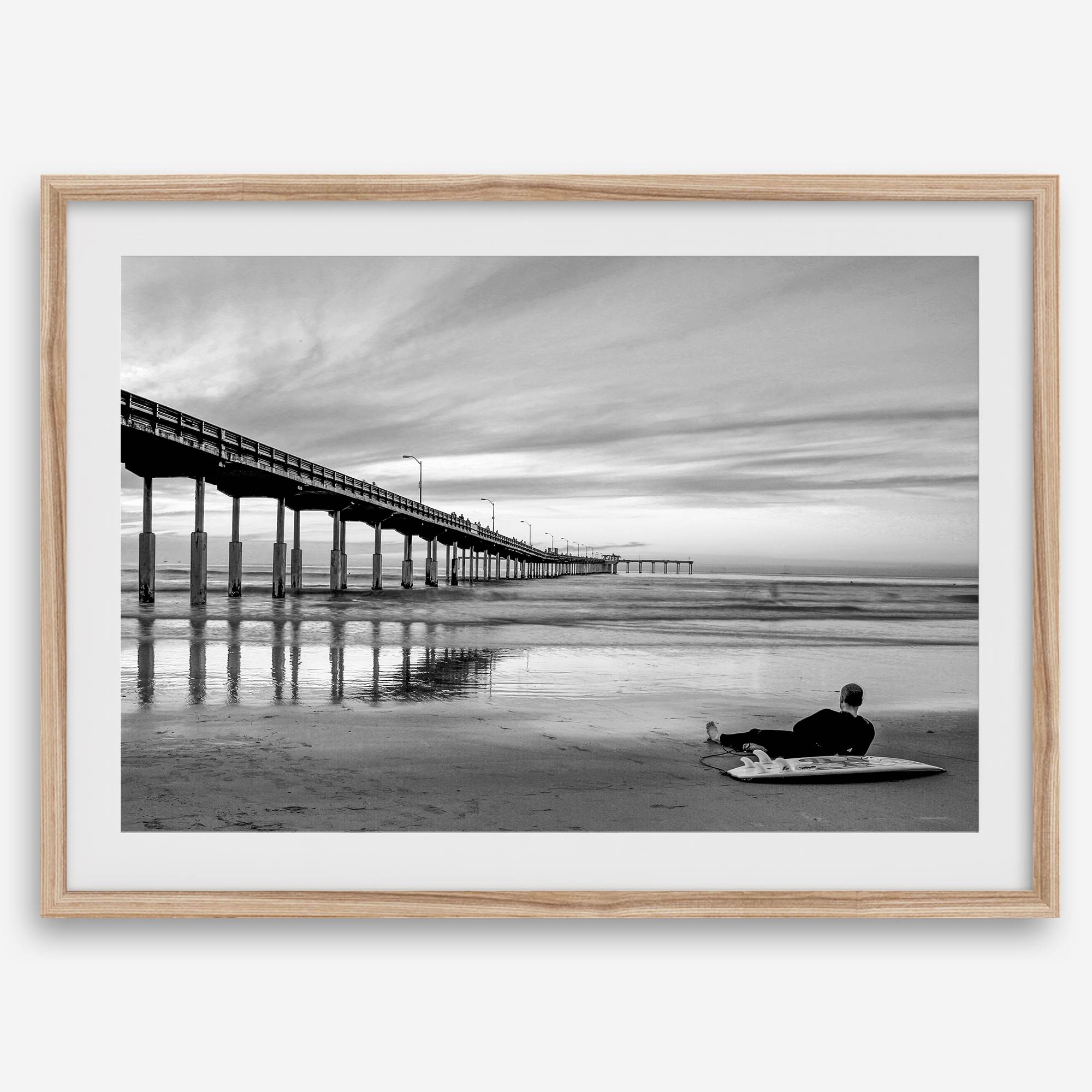 Ocean Beach Pier San Diego photographed in black and white with a lone surfer resting on the shoreline.
