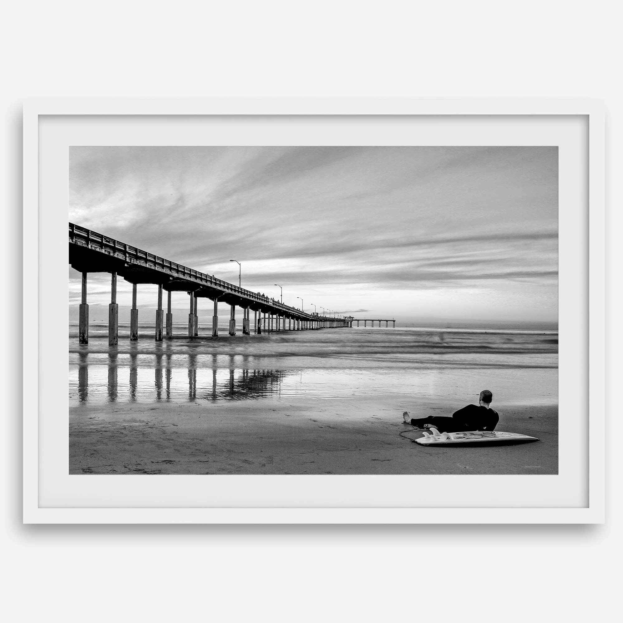 Ocean Beach Pier San Diego photographed in black and white with a lone surfer resting on the shoreline.