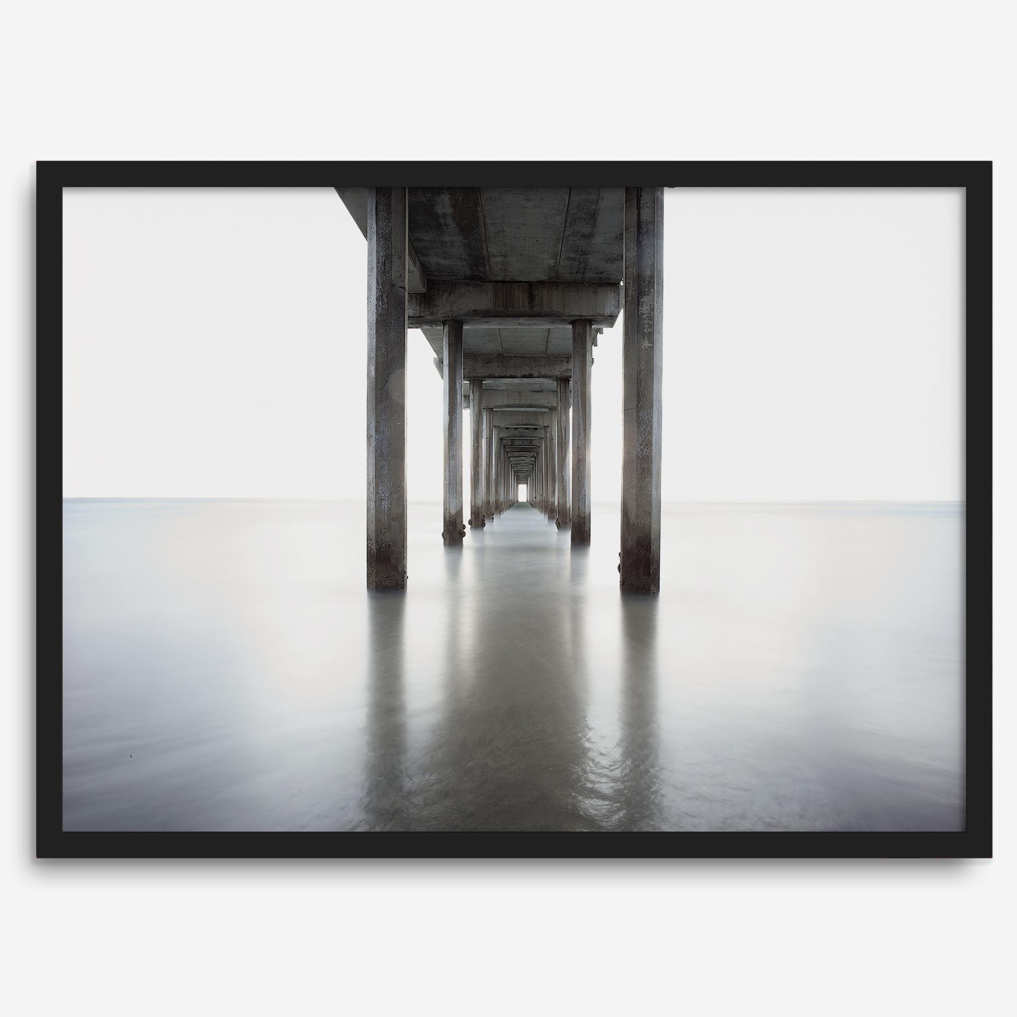 La Jolla coastal photograph looking beneath Scripps Pier toward the Pacific horizon, featuring symmetrical columns and minimalist ocean tones.