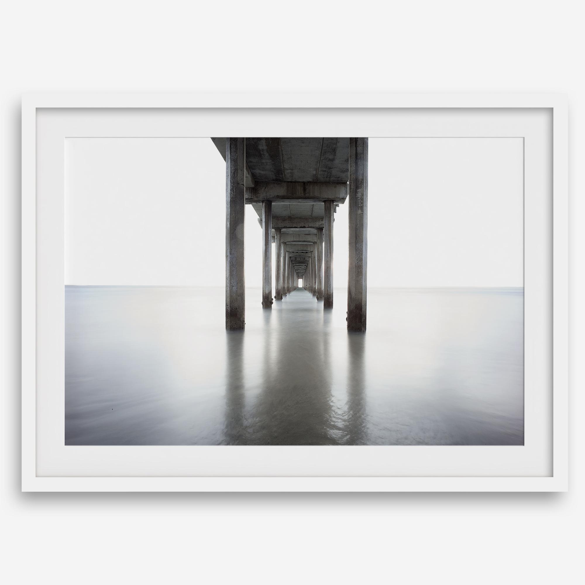 La Jolla coastal photograph looking beneath Scripps Pier toward the Pacific horizon, featuring symmetrical columns and minimalist ocean tones.