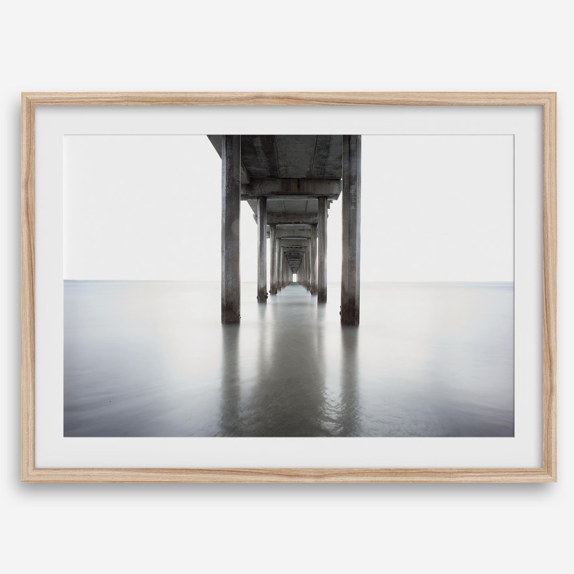 La Jolla coastal photograph looking beneath Scripps Pier toward the Pacific horizon, featuring symmetrical columns and minimalist ocean tones.