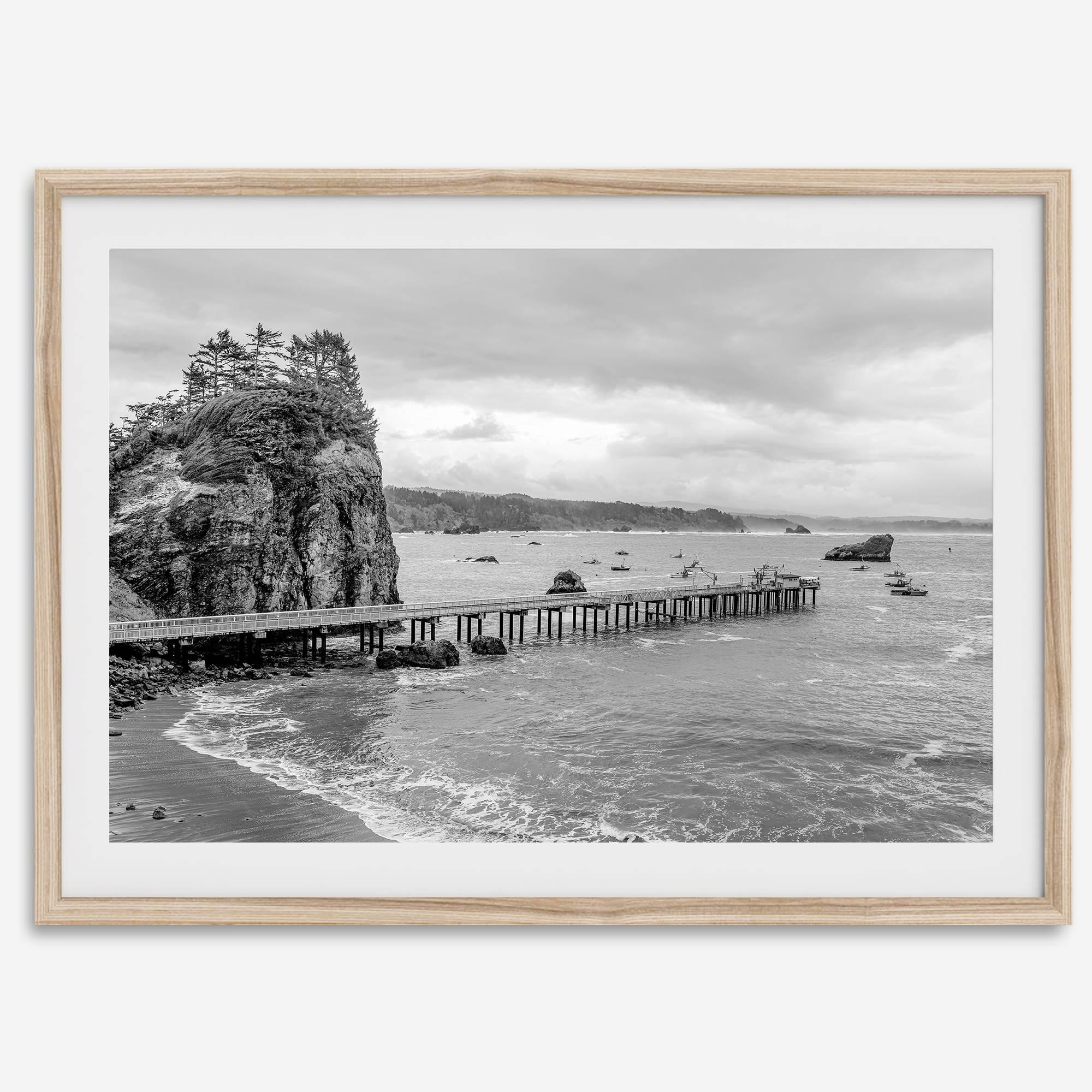 Scenic Pacific Northwest wall art of Trinidad State Park in California in black and white, showcasing a coastal pier, lush green cliffs, and calm ocean waves under cloudy skies.