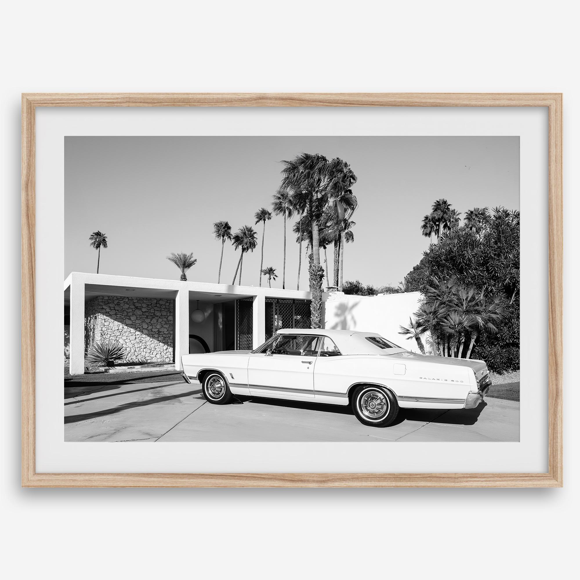 Palm Springs artwork featuring a classic vintage car, mid-century modern architecture and tall desert palm trees in black and white.