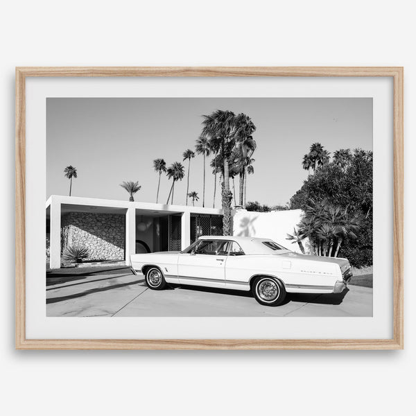Palm Springs artwork featuring a classic vintage car, mid-century modern architecture and tall desert palm trees in black and white.
