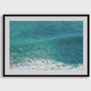 Aerial beach wall art featuring a lone surfer paddling through turquoise ocean waves, with foamy white surf along the shoreline.