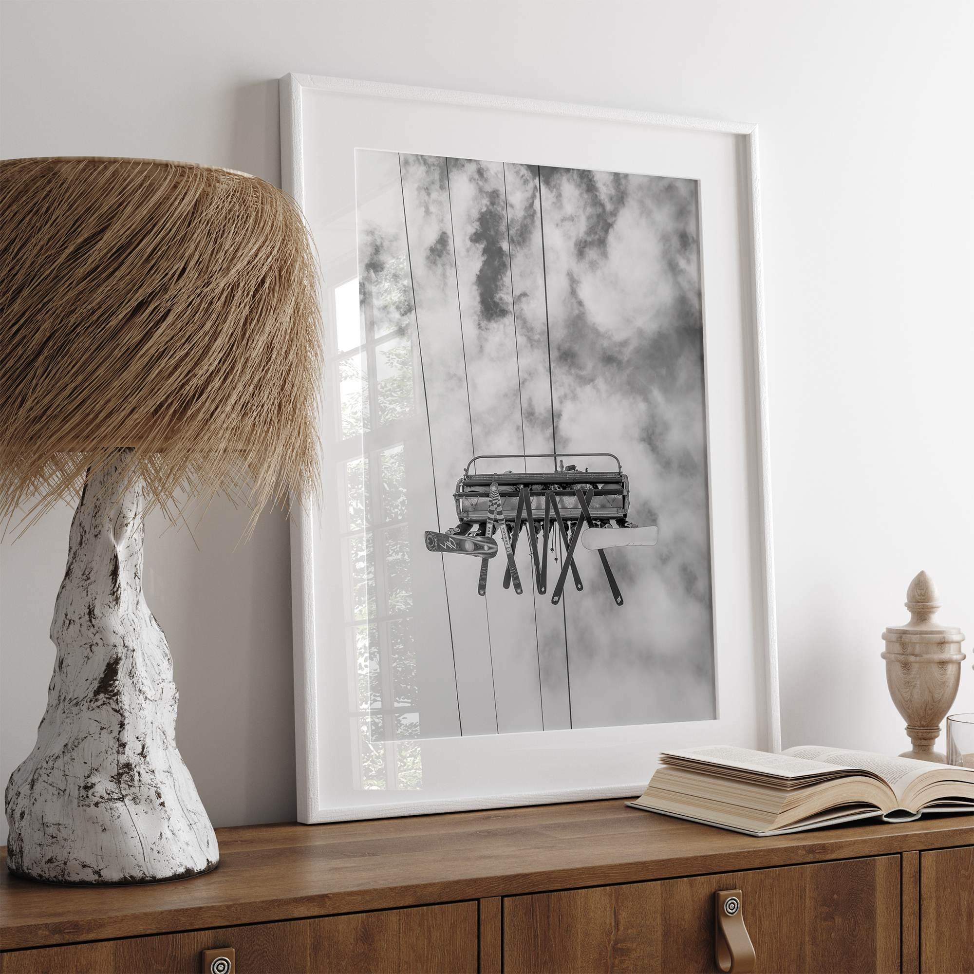 Monochrome ski lift view from below with hanging skis and cloudy mountain sky background.