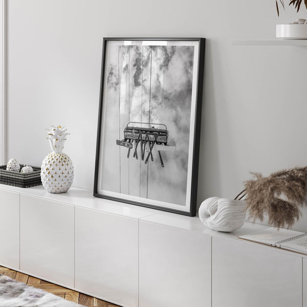 Monochrome ski lift view from below with hanging skis and cloudy mountain sky background.