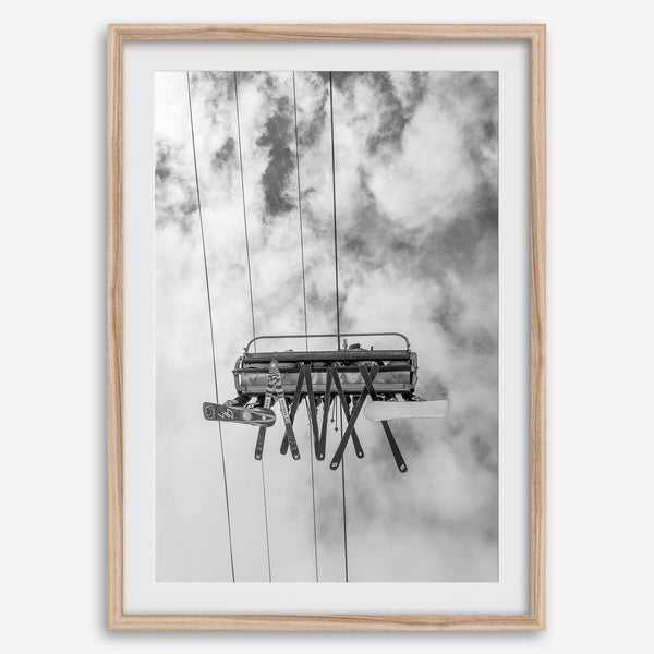 Monochrome ski lift view from below with hanging skis and cloudy mountain sky background.