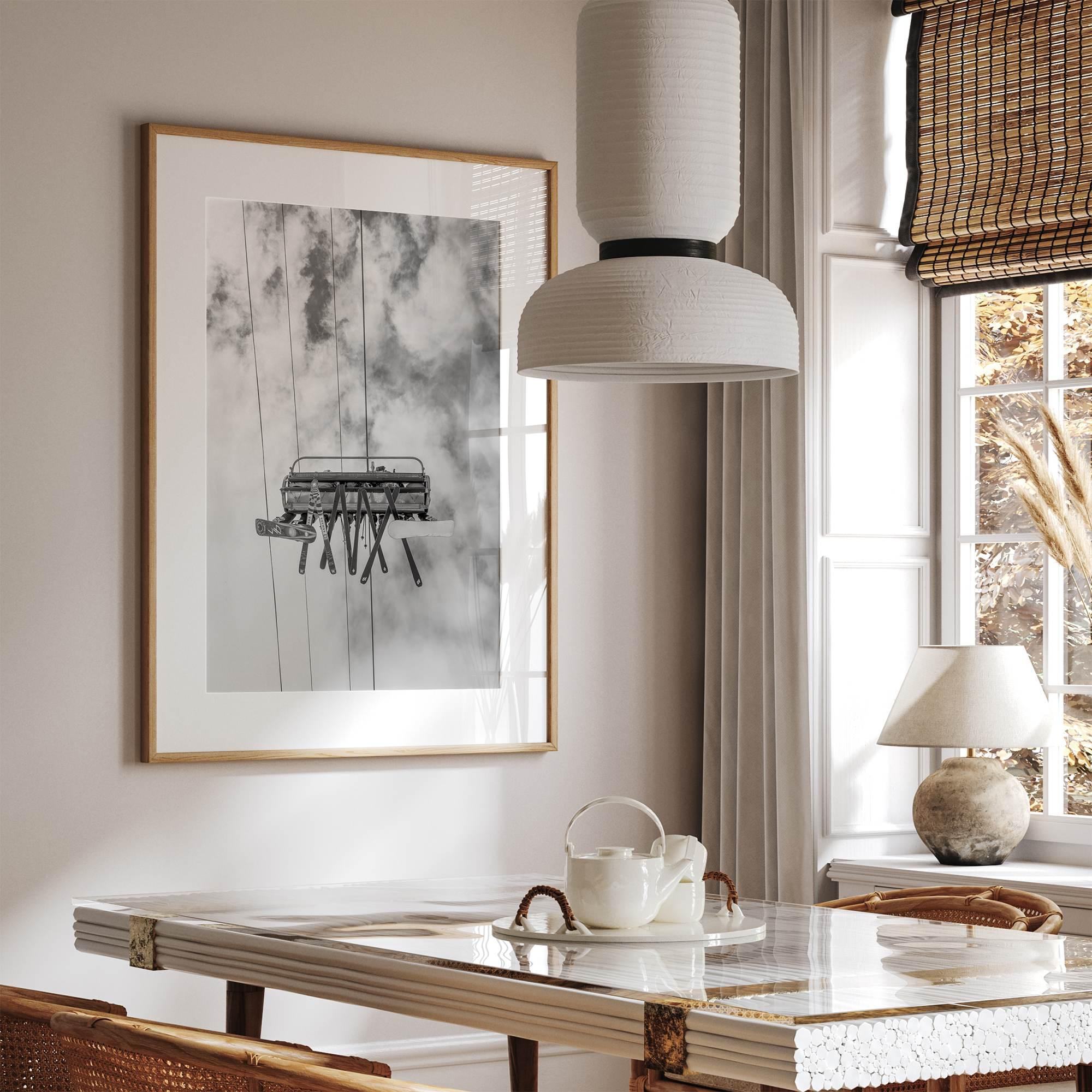 Monochrome ski lift view from below with hanging skis and cloudy mountain sky background.