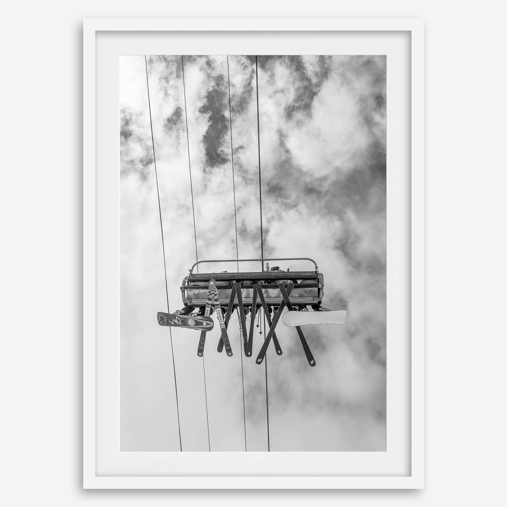 Monochrome ski lift view from below with hanging skis and cloudy mountain sky background.