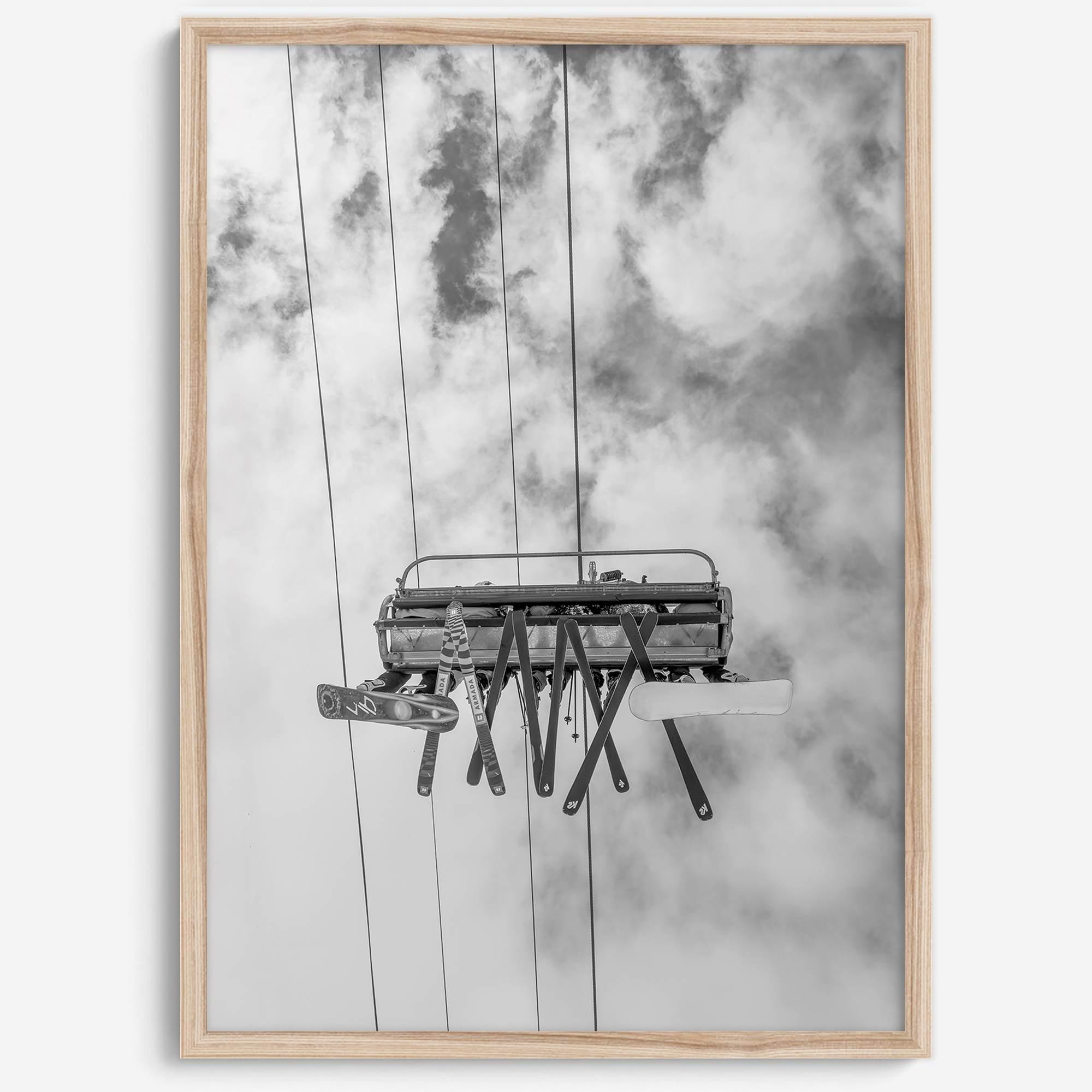 Monochrome ski lift view from below with hanging skis and cloudy mountain sky background.
