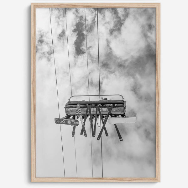 Monochrome ski lift view from below with hanging skis and cloudy mountain sky background.