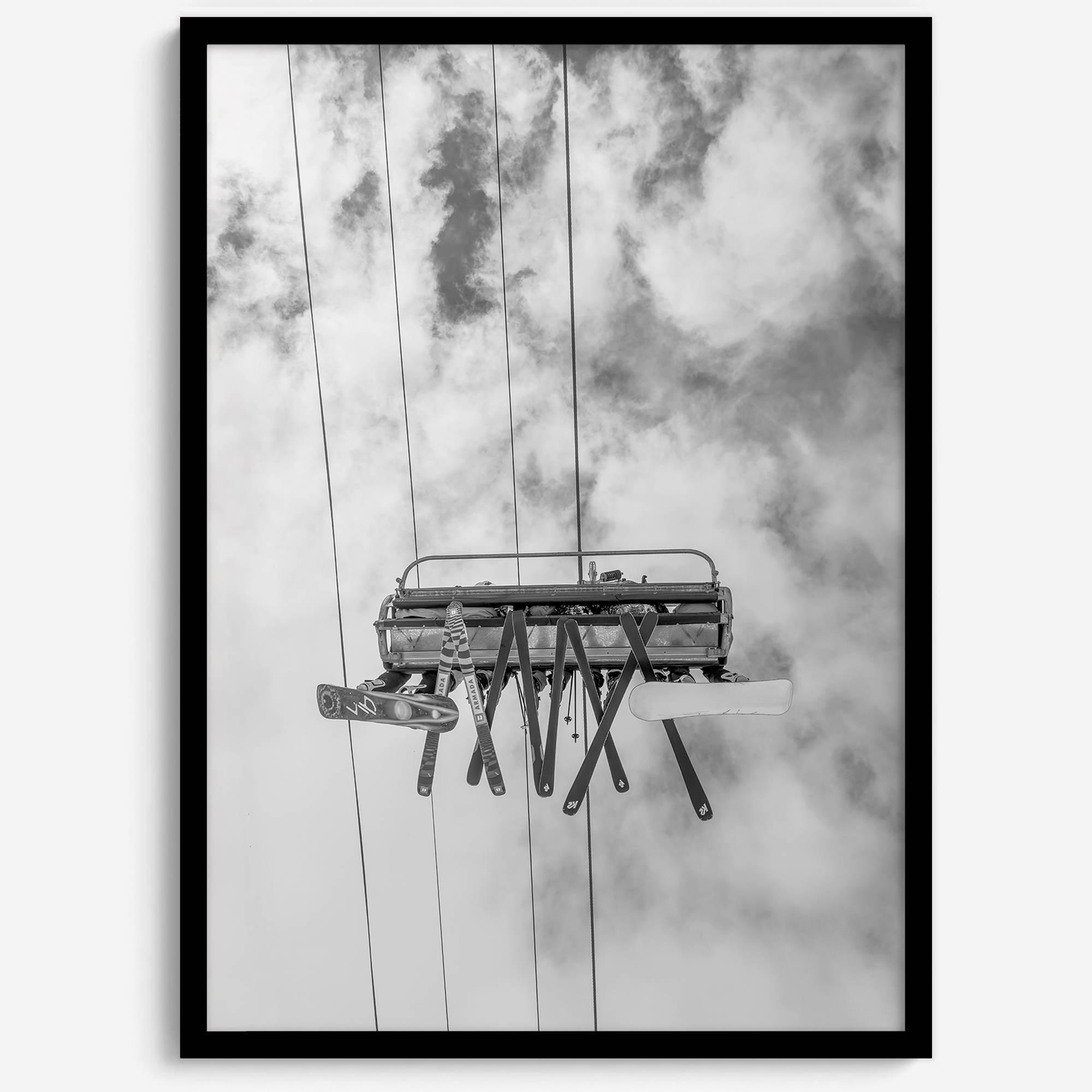 Monochrome ski lift view from below with hanging skis and cloudy mountain sky background.