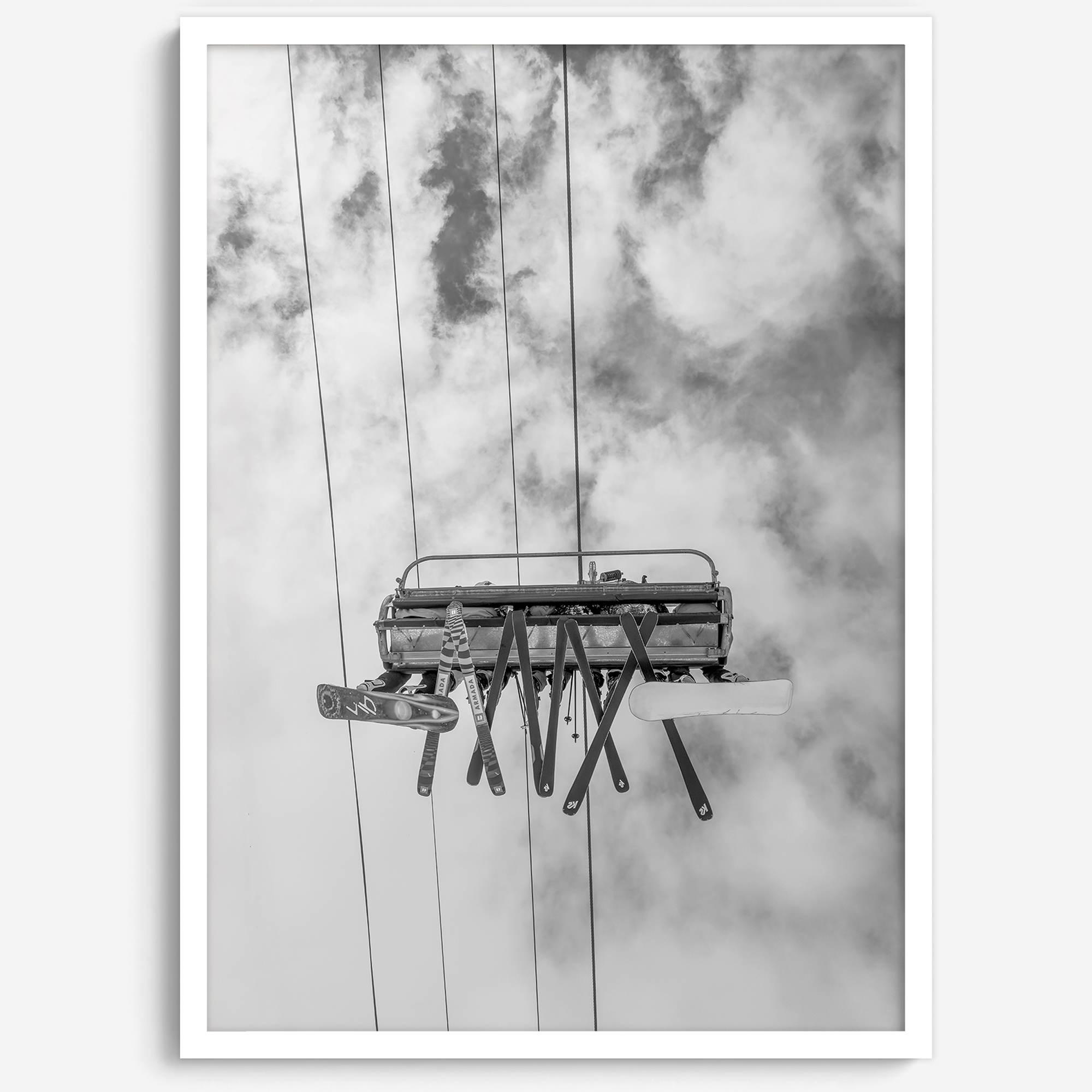 Monochrome ski lift view from below with hanging skis and cloudy mountain sky background.