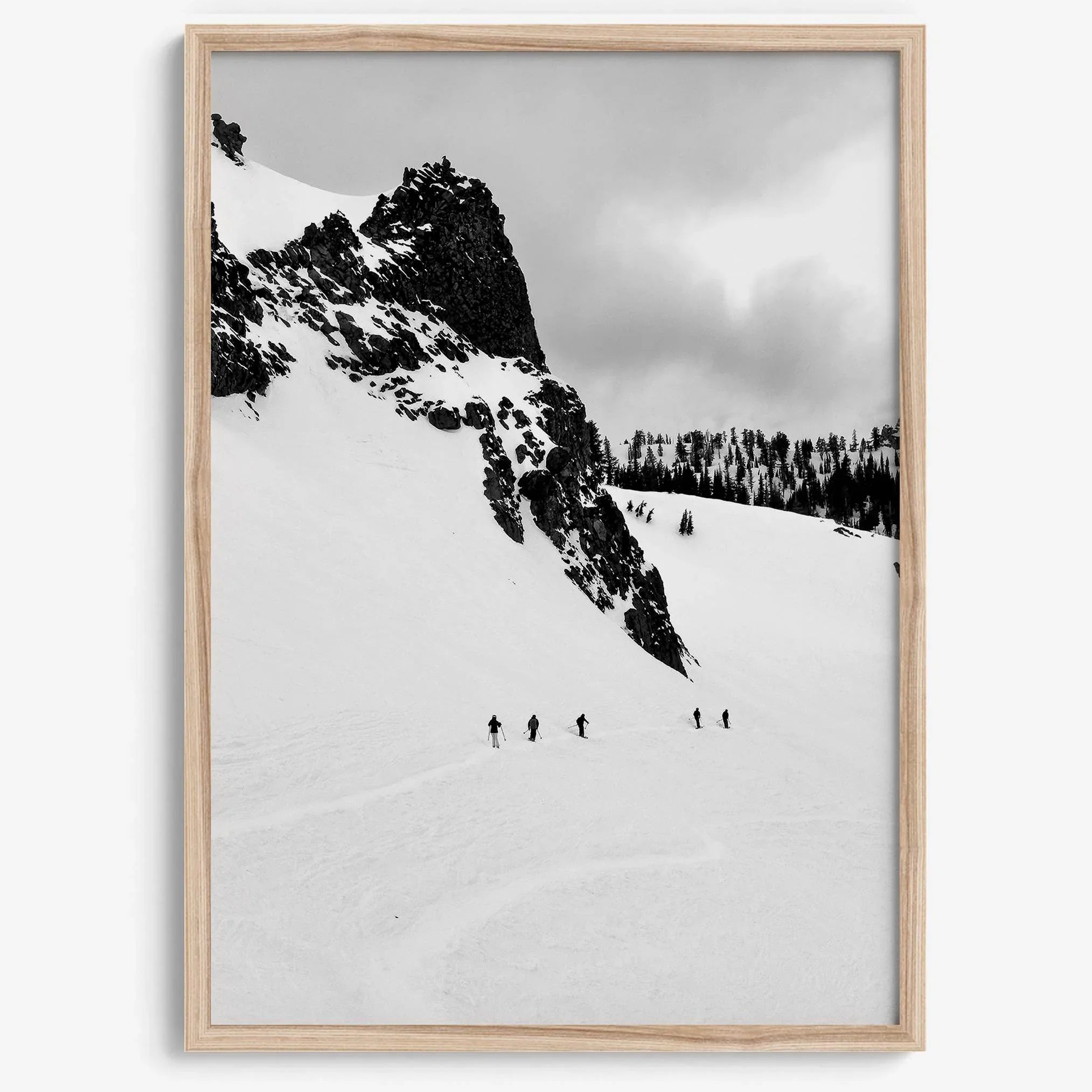 A fine art print showing five skiers traversing a vast, snowy mountain landscape under a pale winter sky, surrounded by untouched wilderness.