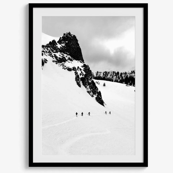 A fine art print showing five skiers traversing a vast, snowy mountain landscape under a pale winter sky, surrounded by untouched wilderness.