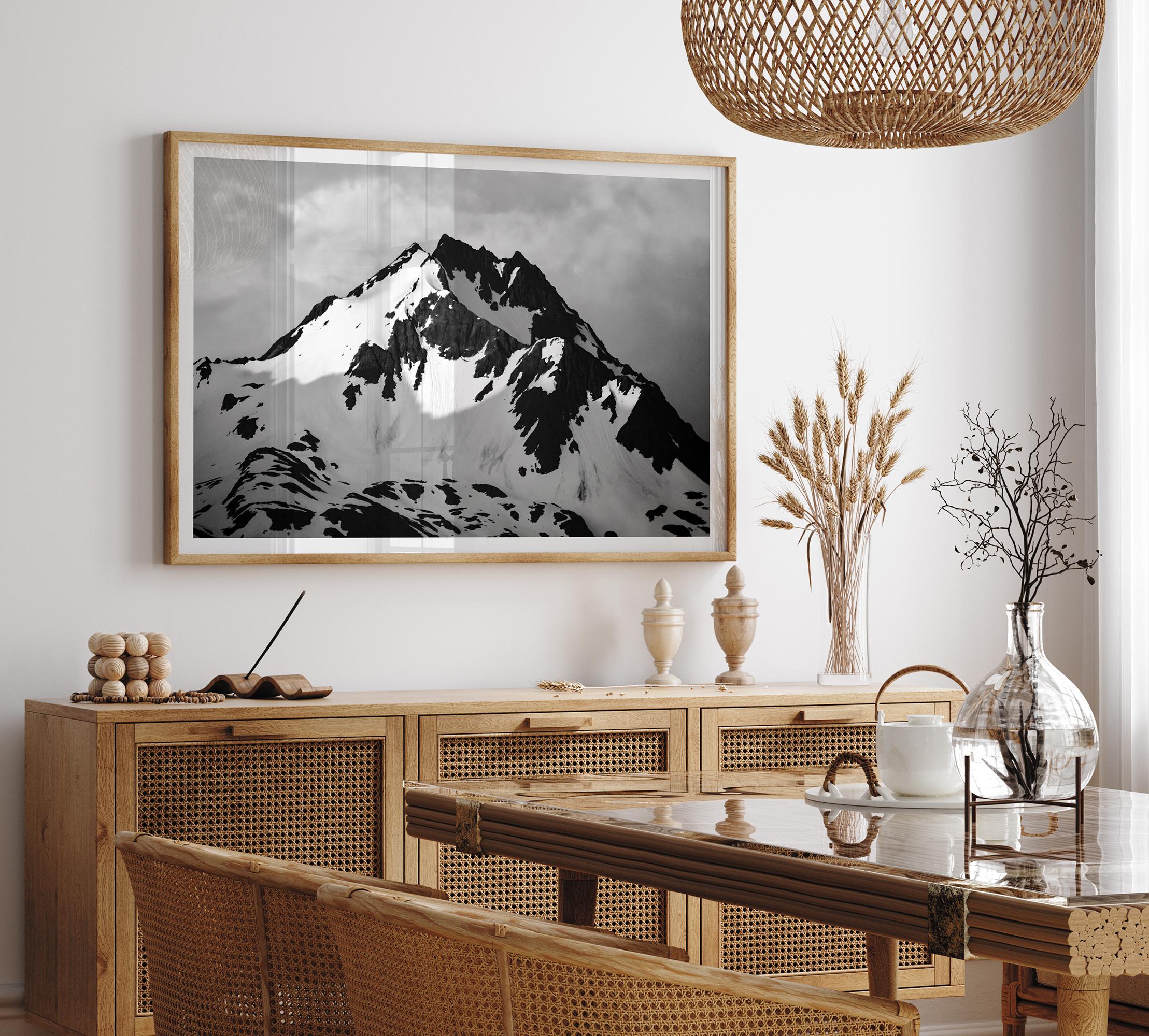 Black and white fine art photograph of a snowy Alaska mountain rising above coastal waters beneath dramatic clouds.