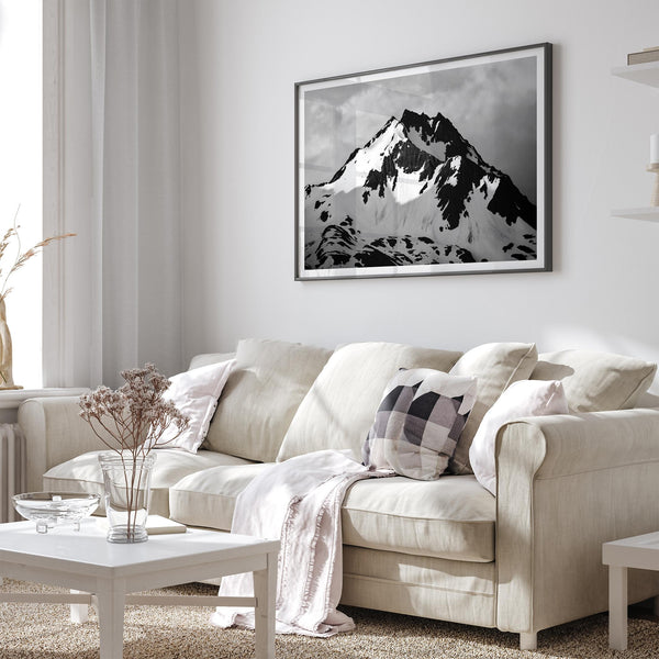 Black and white fine art photograph of a snowy Alaska mountain rising above coastal waters beneath dramatic clouds.