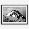 Black and white fine art photograph of a snowy Alaska mountain rising above coastal waters beneath dramatic clouds.