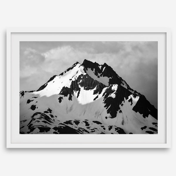 Black and white fine art photograph of a snowy Alaska mountain rising above coastal waters beneath dramatic clouds.