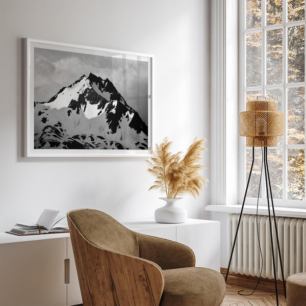 Black and white fine art photograph of a snowy Alaska mountain rising above coastal waters beneath dramatic clouds.
