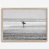 Black and white surfer photography showing a lone surfer on the beach, with waves in the background, capturing minimalist coastal beauty.