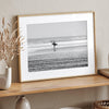 Black and white surfer photography showing a lone surfer on the beach, with waves in the background, capturing minimalist coastal beauty.