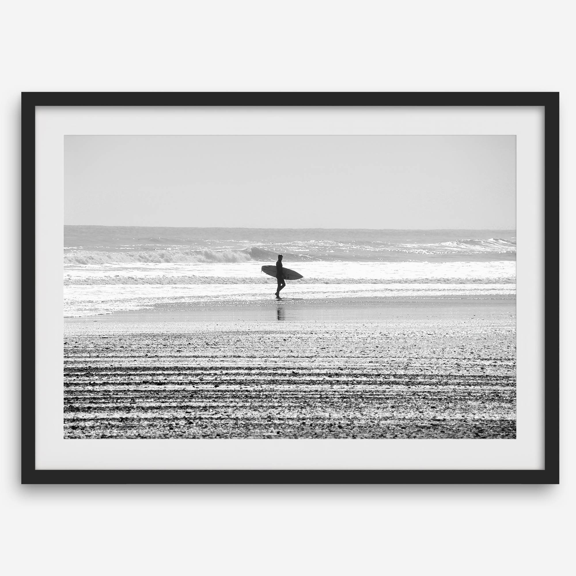 Black and white surfer photography showing a lone surfer on the beach, with waves in the background, capturing minimalist coastal beauty.