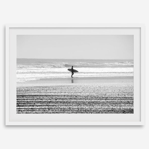 Black and white surfer photography showing a lone surfer on the beach, with waves in the background, capturing minimalist coastal beauty.