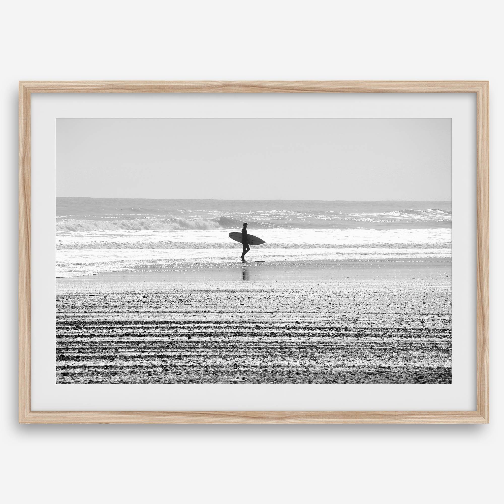 Black and white surfer photography showing a lone surfer on the beach, with waves in the background, capturing minimalist coastal beauty.