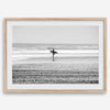 Black and white surfer photography showing a lone surfer on the beach, with waves in the background, capturing minimalist coastal beauty.