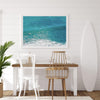Aerial beach wall art featuring a lone surfer paddling through turquoise ocean waves, with foamy white surf along the shoreline.