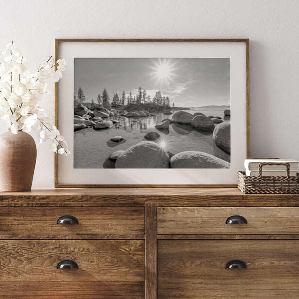 Capture the beauty of Lake Tahoe with this stunning black and white lake wall art. The image showcases majestic rocks rising from crystal-clear water. The reflection of the sun in the water adds a magical touch to the breathtaking scenery.